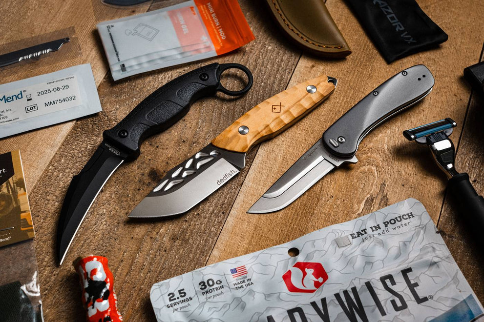 Crate Club gear flatlay: three folding knives, first aid burn gel, sheath, and freeze-dried meal pouch